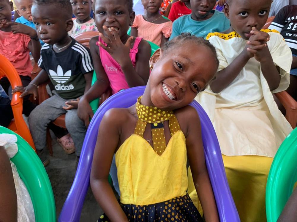 Menina sorrindo entre outras crianças sentadas em cadeiras coloridas