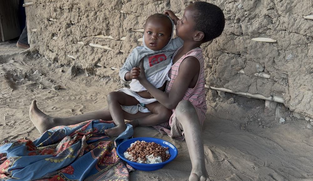 Menina sentada segurando um bebê ao lado de um prato de comida