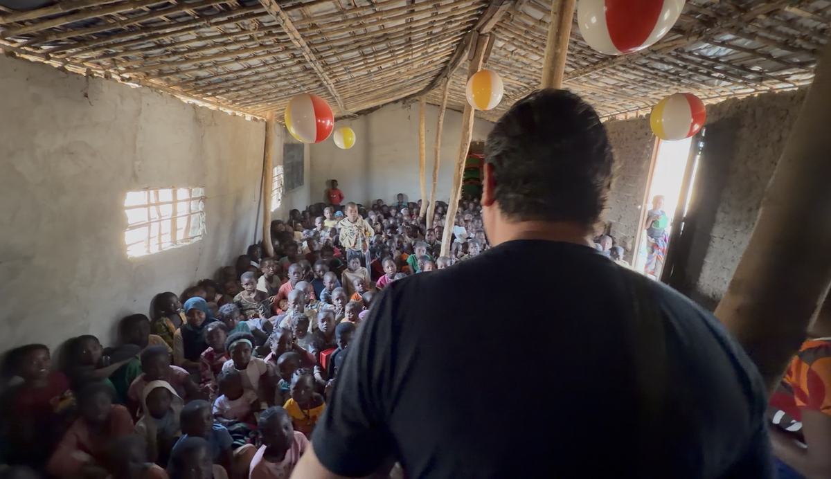 Centenas de crianças reunidas dentro do templo de paredes de barro e cobertura de bambu